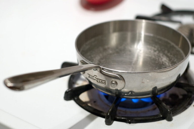 A stainless steel saucepan on a lit gas stove with water boiling inside.