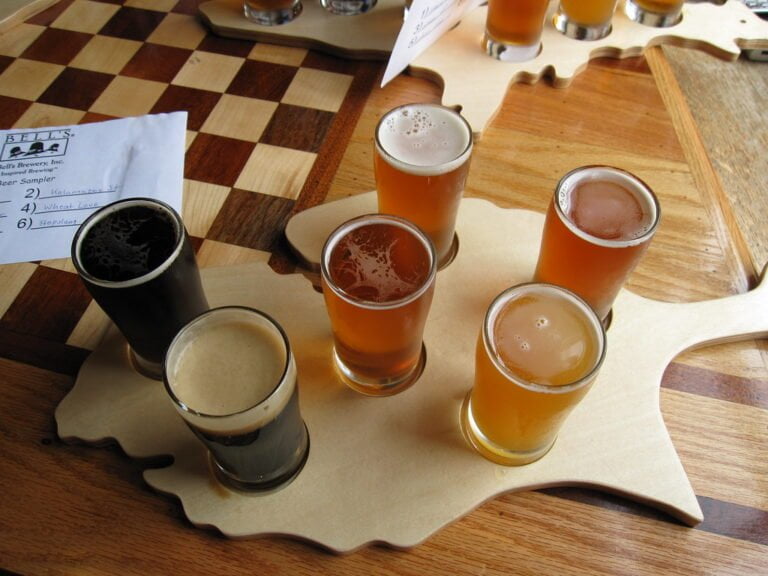 A flight of five different beers served in small glasses on a wooden paddle, with a beer menu on the table.