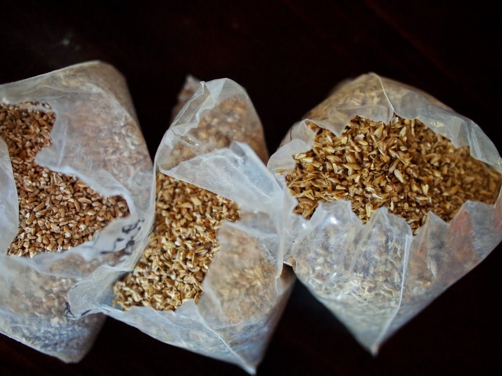 Three open bags of various grains on a dark surface.