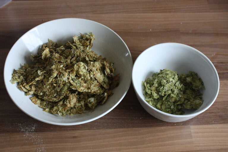 Two bowls of hops on a wooden surface, the larger bowl containing more hops than the smaller bowl.