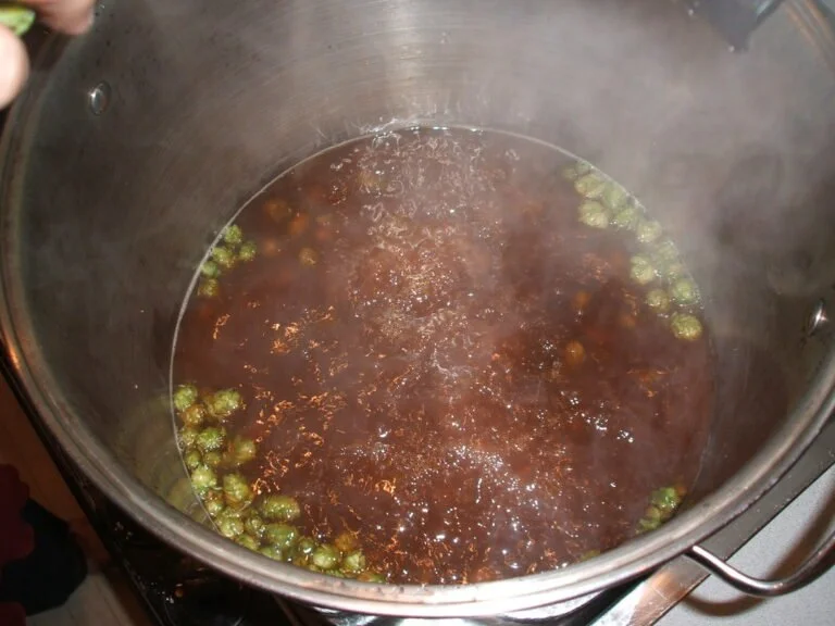 A large metal pot with boiling liquid and hops, likely brewing beer.