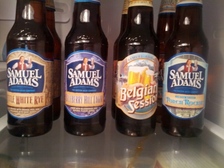 Four bottles of Samuel Adams beer, displaying different flavors, placed in a refrigerator.