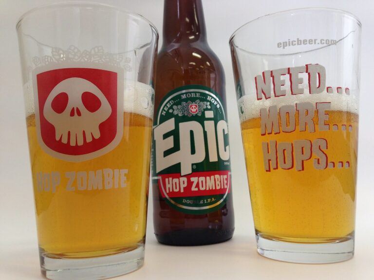 Two glasses of beer with printed text "HOP ZOMBIE" and "NEED... MORE... HOPS..." on them, flanking a bottle labeled "Epic HOP ZOMBIE Double IPA."