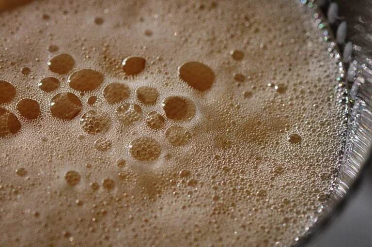 A close-up view of various-sized bubbles formed on the surface of a liquid, possibly a fizzy beverage, with a shallow depth of field focusing on the larger bubbles.