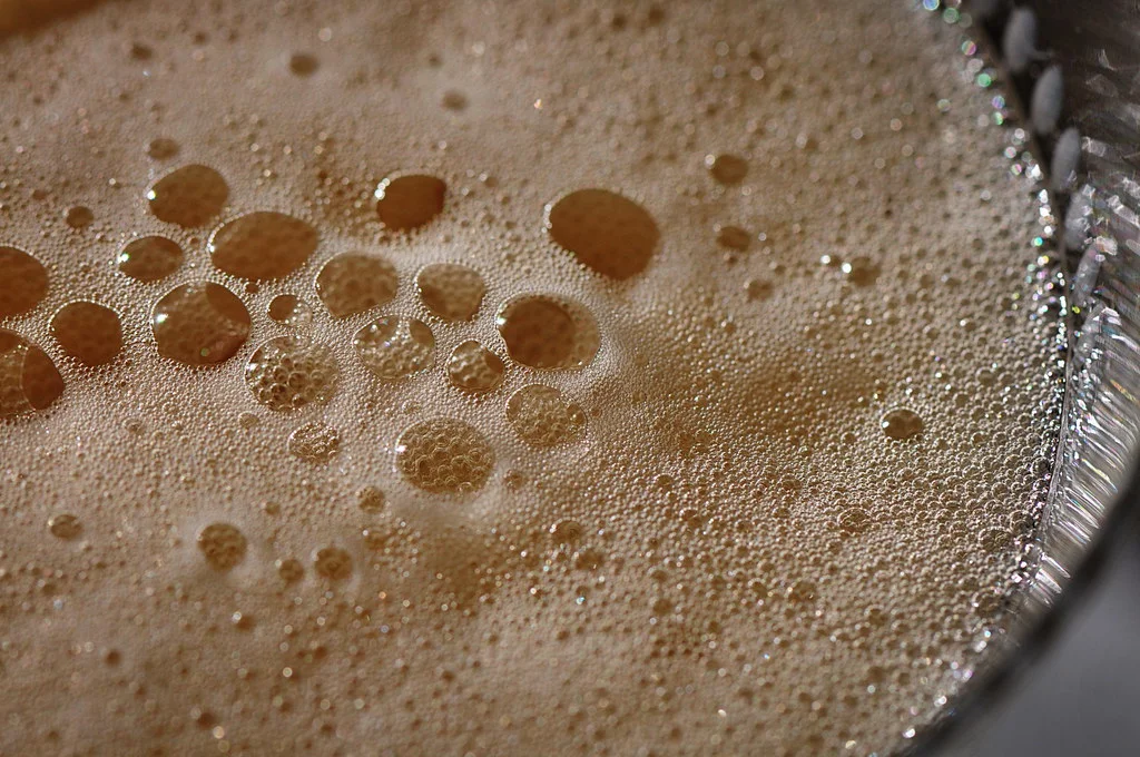 A close-up view of various-sized bubbles formed on the surface of a liquid, possibly a fizzy beverage, with a shallow depth of field focusing on the larger bubbles.