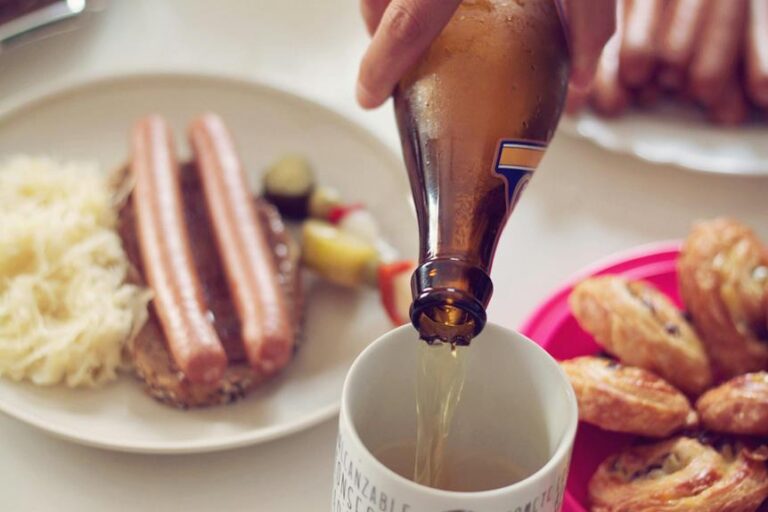 A person pouring beer into a mug with traditional German food, including sausages and sauerkraut, on the table.