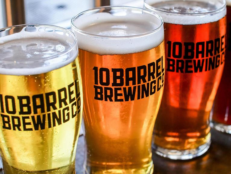 Three glasses of beer with varying shades of amber, carrying the logo "10 Barrel Brewing Co.," displayed in a row on a table.