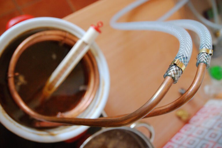 A close-up of a copper immersion wort chiller with tubing attached, used in homebrewing, positioned above a pot of wort.