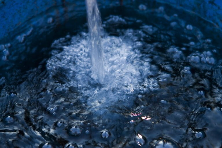 Water pouring into a blue container, causing bubbles and ripples on the surface.