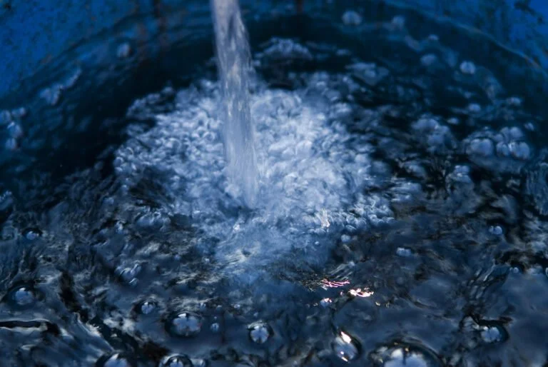Water pouring into a blue container, causing bubbles and ripples on the surface.