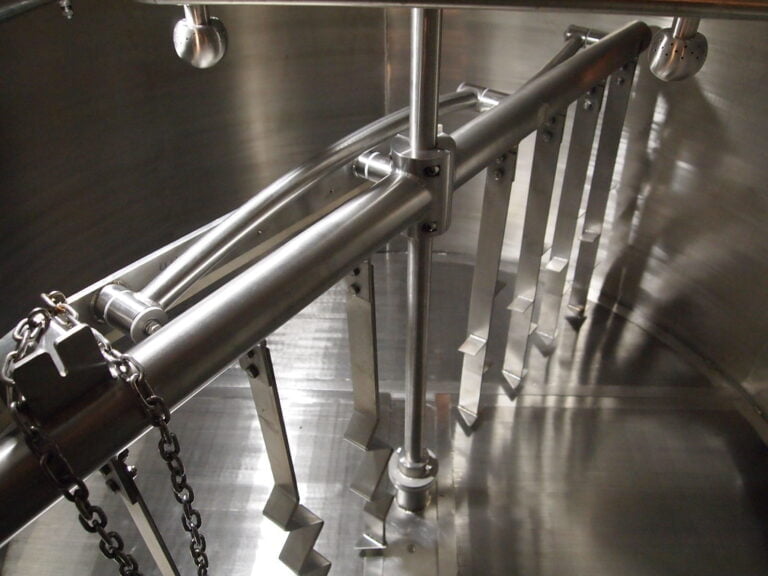 Stainless steel turnstile with metal bars and chains on a reflective surface.