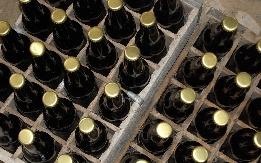 Aerial view of dark glass bottles with golden caps organized in a wooden crate.