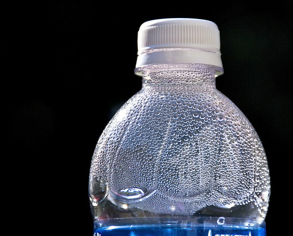 A plastic water bottle covered in condensation droplets against a dark background.