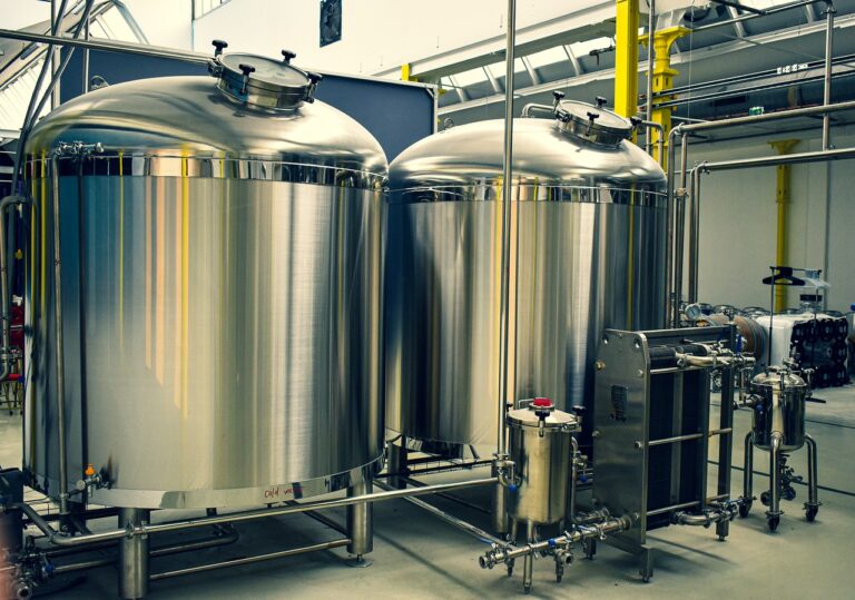 Two large stainless steel fermentation tanks with associated piping and valves in a brewery or industrial setting.