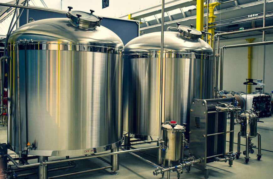Two large stainless steel fermentation tanks with attached pipes and control valves in a brewery setting.