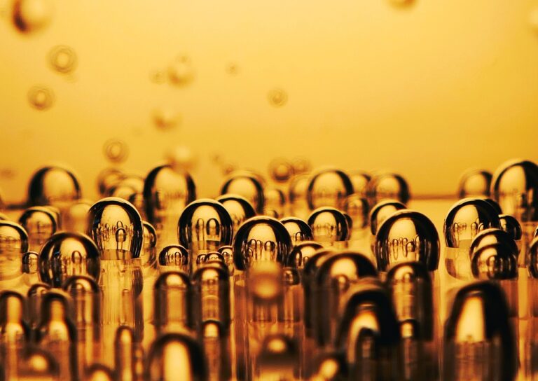 A close-up of multiple clear round water droplets on a golden-hued surface, with reflections visible inside each drop.