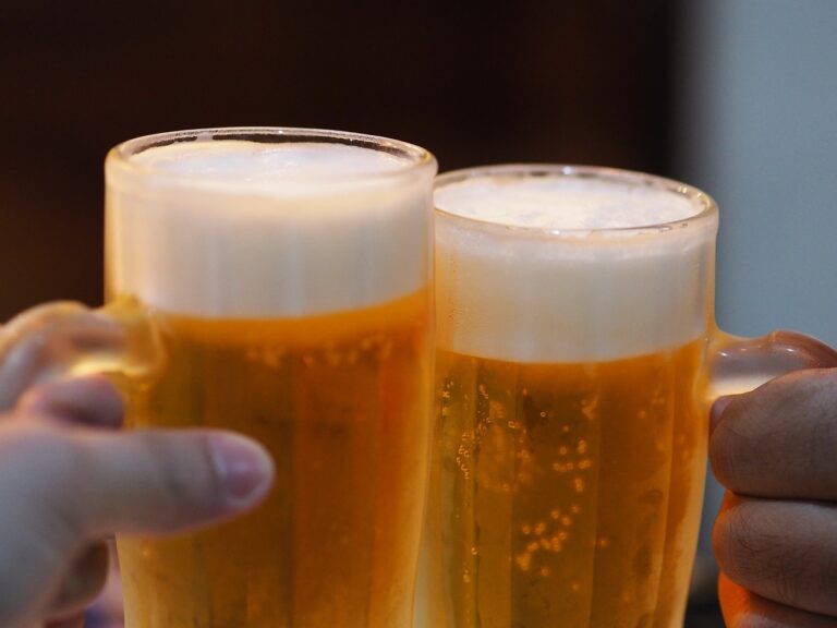Two hands holding frosty mugs of beer with foamy tops.