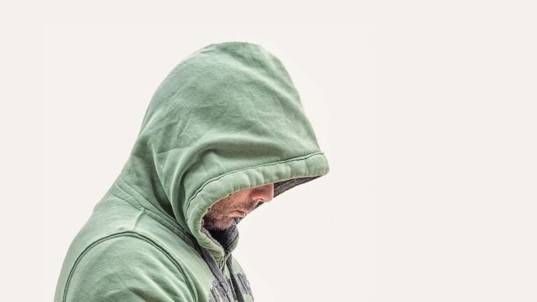 A person in a green hooded sweatshirt looking down, against a white background.