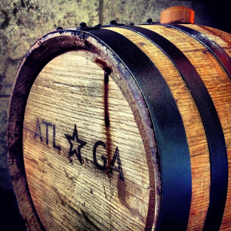 A close-up of a wooden barrel with the inscription "ATL GA" and a star, showing signs of liquid seepage.