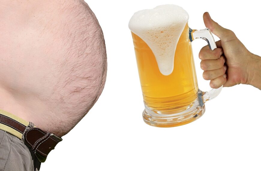 A close-up image split between a man's protruding belly on the left and a hand holding a large mug of beer with frothy head on the right, against a white background.