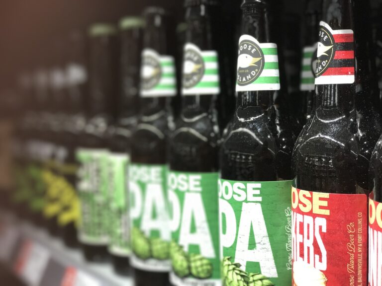 Row of Goose Island IPA beer bottles on a shelf with a shallow depth of field, focusing on one bottle with a green label in the foreground.