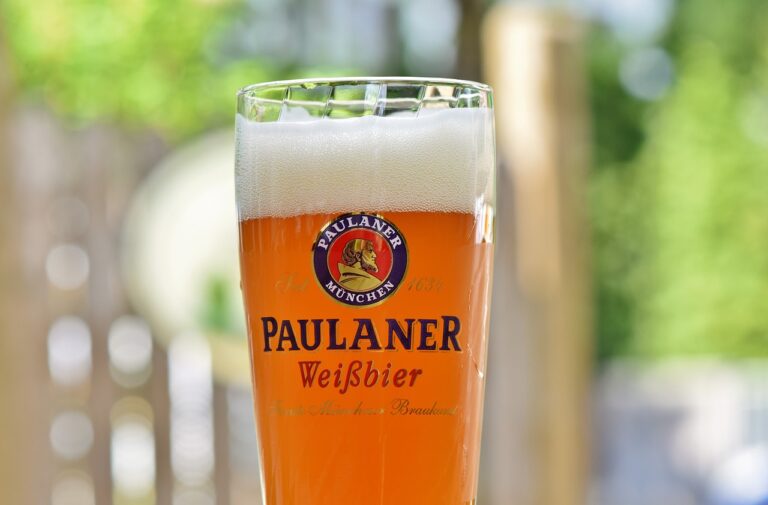 A glass of Paulaner Weißbier with a frothy head, set against an out-of-focus green natural background.