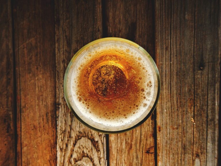 A top view of a full glass of beer with frothy head, placed on a rustic wooden surface.
